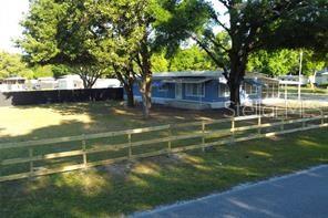 A blue mobile home sits behind a wooden fence on a grassy lot with trees — 8047 CINDY DRIVE, ZEPHYRHILLS, FL