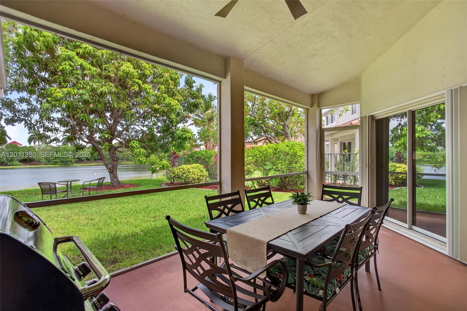 A screened-in patio features a dining set, a grill, and views of a lake — 370 Carrington Dr, Weston FL 33326, WESTON, FL
