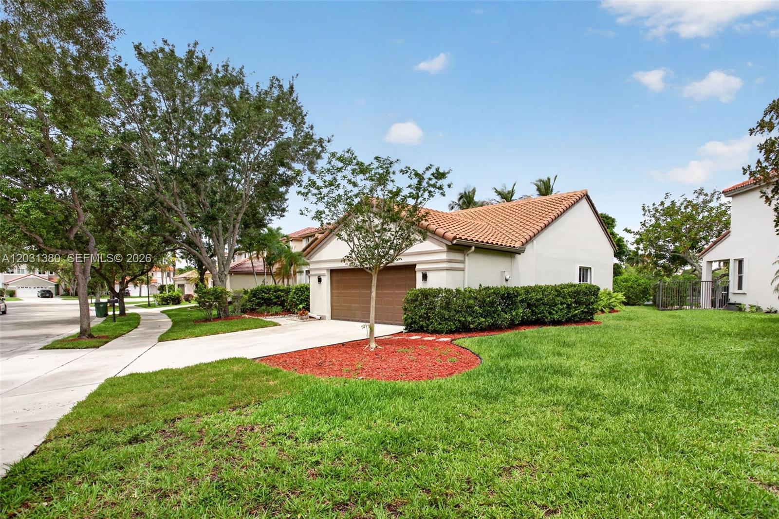 A single-story house with a brown garage door, tile roof, and a landscaped front yard — 370 Carrington Dr, Weston FL 33326, WESTON, FL