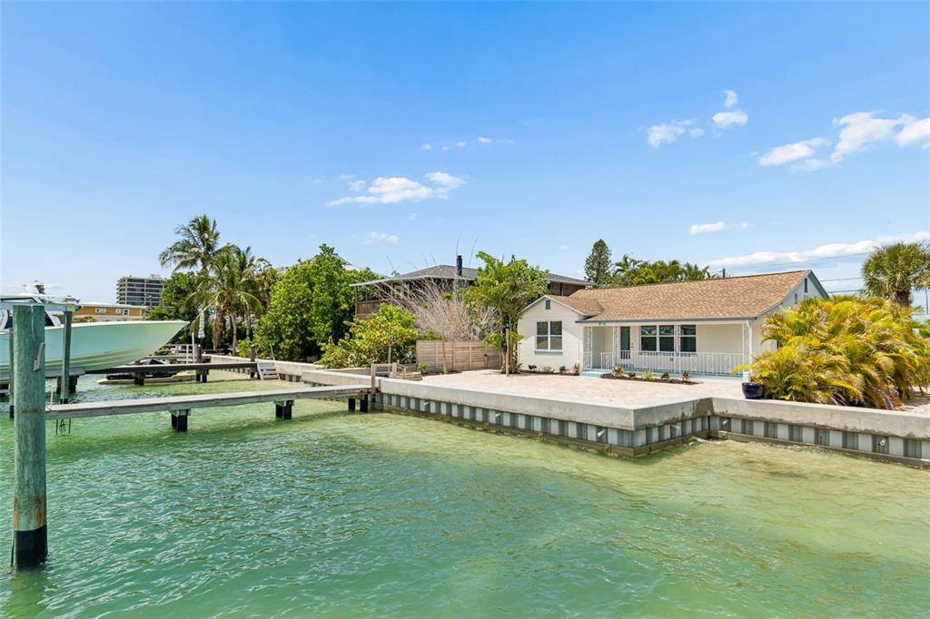 A waterfront house with a boat dock and a gravel yard under a blue sky — 8125 BAYSHORE DRIVE, TREASURE ISLAND, FL