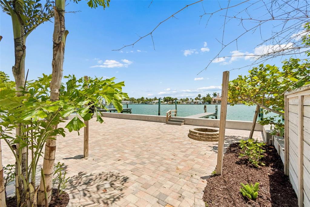 A paved patio with a fire pit overlooks a canal with a private boat dock — 8125 BAYSHORE DRIVE, TREASURE ISLAND, FL