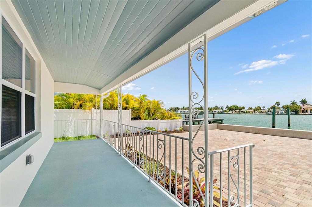 A covered porch with blue flooring overlooks a brick patio and a waterfront canal — 8125 BAYSHORE DRIVE, TREASURE ISLAND, FL