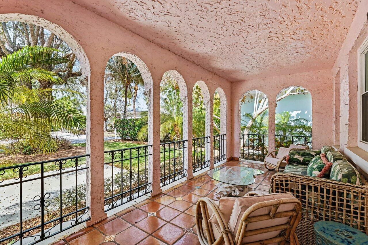 A pink covered porch features arched openings, wrought iron railings, and wicker furniture on tile floors — 217 SE Coconut Avenue, Stuart FL 34996, STUART, FL