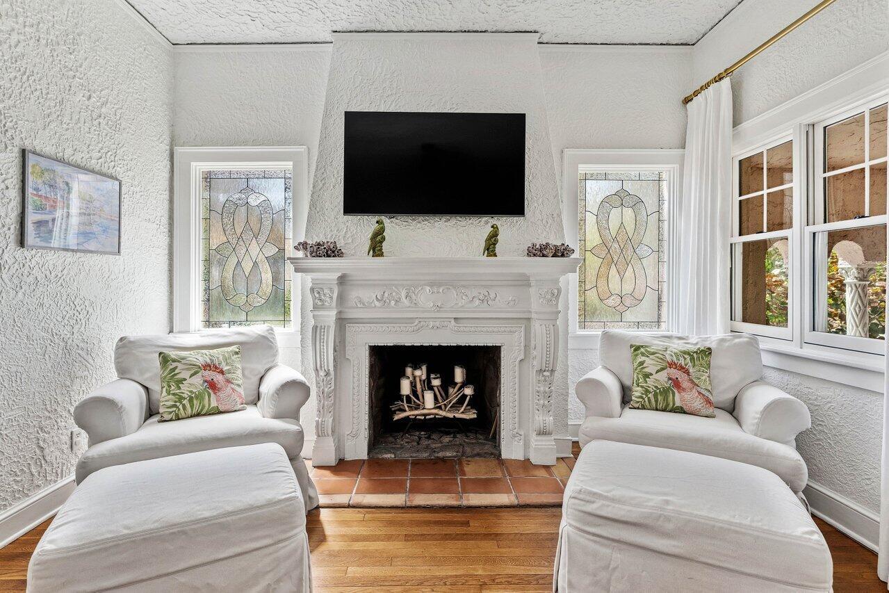 A white fireplace with a mounted television sits between two stained-glass windows and armchairs — 217 SE Coconut Avenue, Stuart FL 34996, STUART, FL