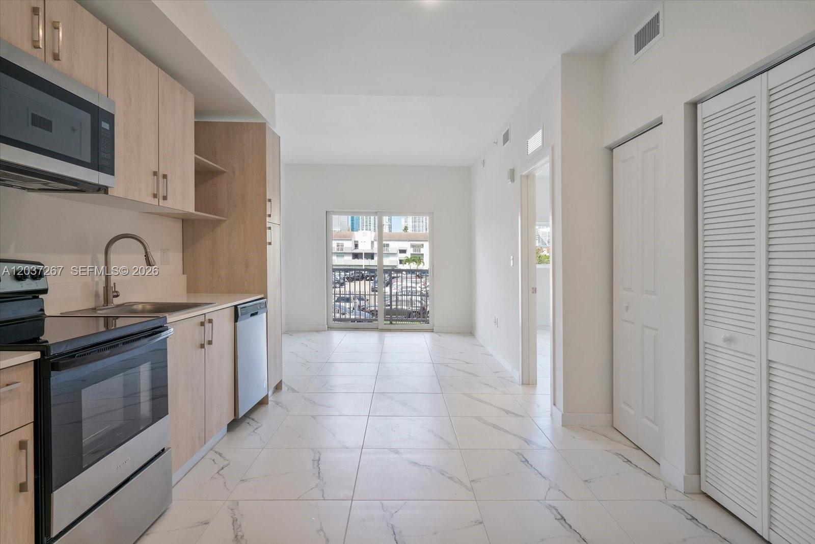 A kitchen with light wood cabinets and marble-look tile flooring leads to a balcony door — 420 SW 7th Ave # 204, Miami FL 33130, MIAMI, FL