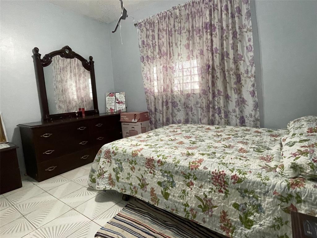 A bedroom features a floral bedspread, a dark wood dresser with a mirror, and tiled floors — CANIACO RIO ABAJO STRD 123, 8201 SECTOR VENDREL, UTUADO, PR