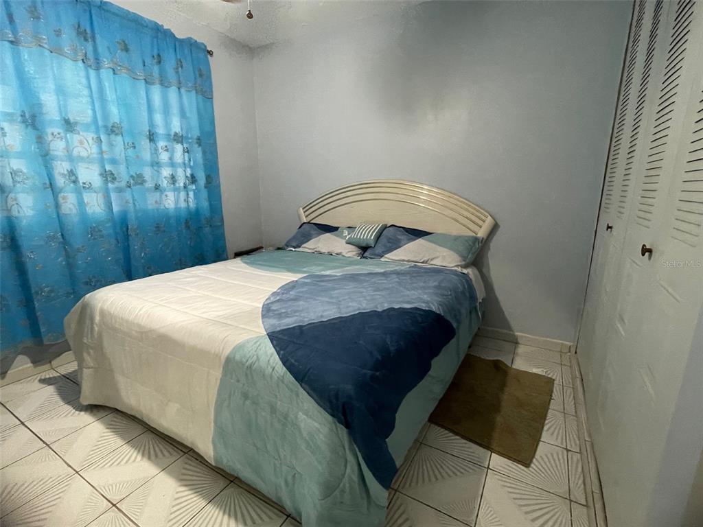 A bedroom features a bed with a blue and white comforter, tiled floors, and curtains — CANIACO RIO ABAJO STRD 123, 8201 SECTOR VENDREL, UTUADO, PR