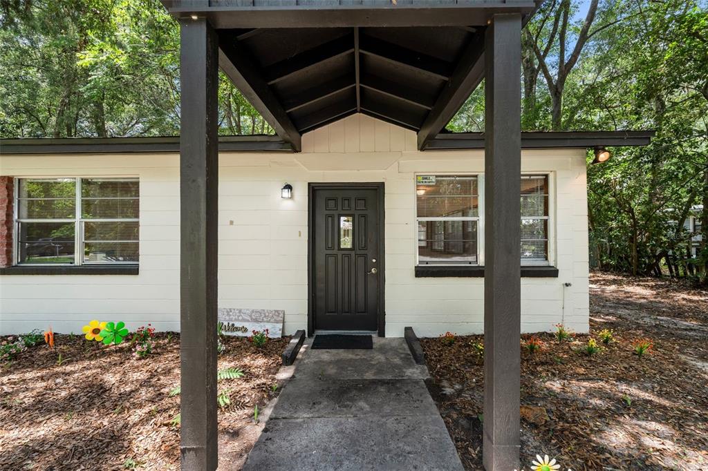 A white house exterior features a dark front door under a covered entryway with columns — 4156 NW 10TH STREET, GAINESVILLE, FL