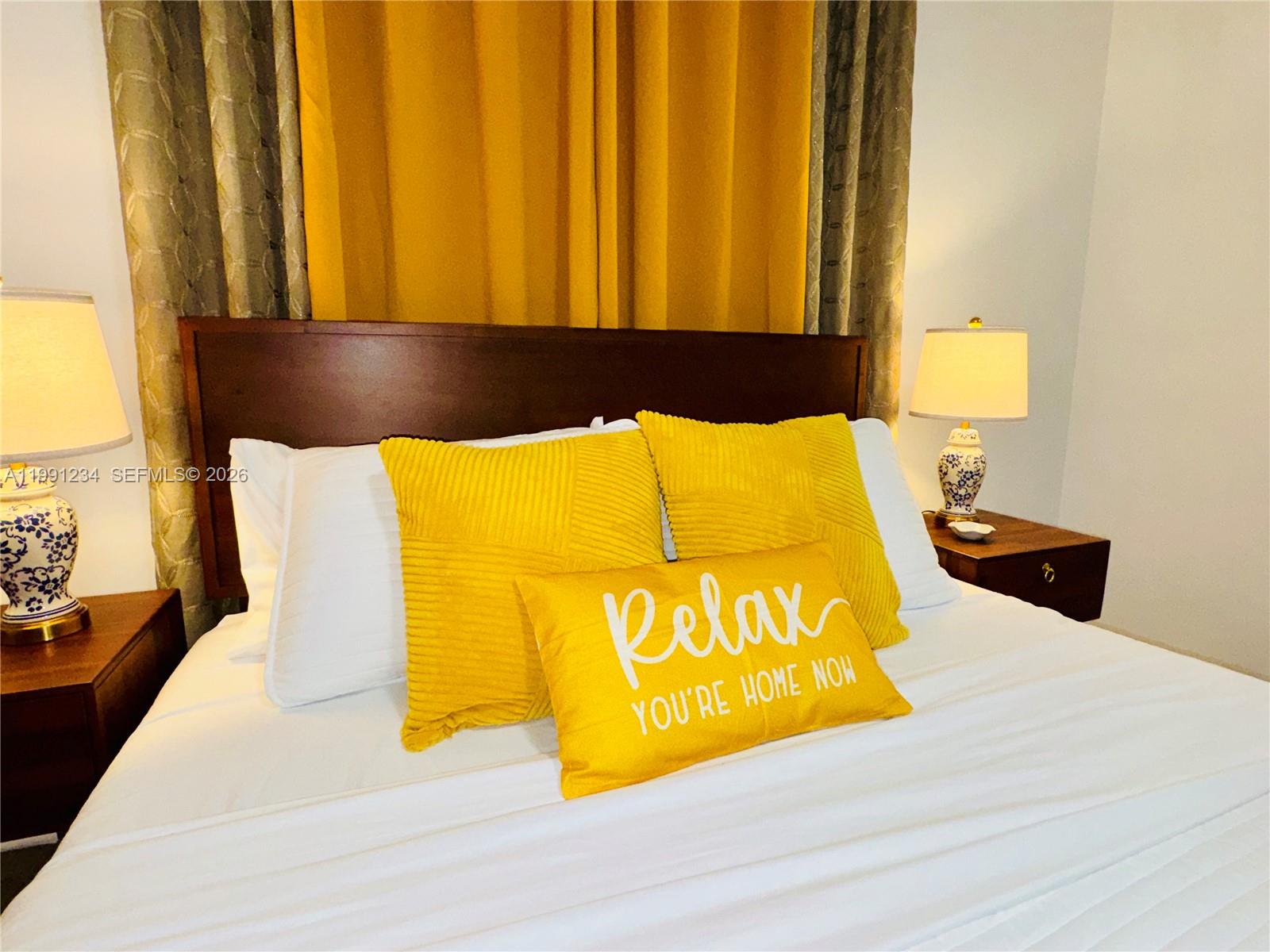 A bedroom features a bed with yellow accent pillows, a dark headboard, and bedside lamps — 5100 Rilma Ave # 0, Sarasota FL 34234, SARASOTA, FL