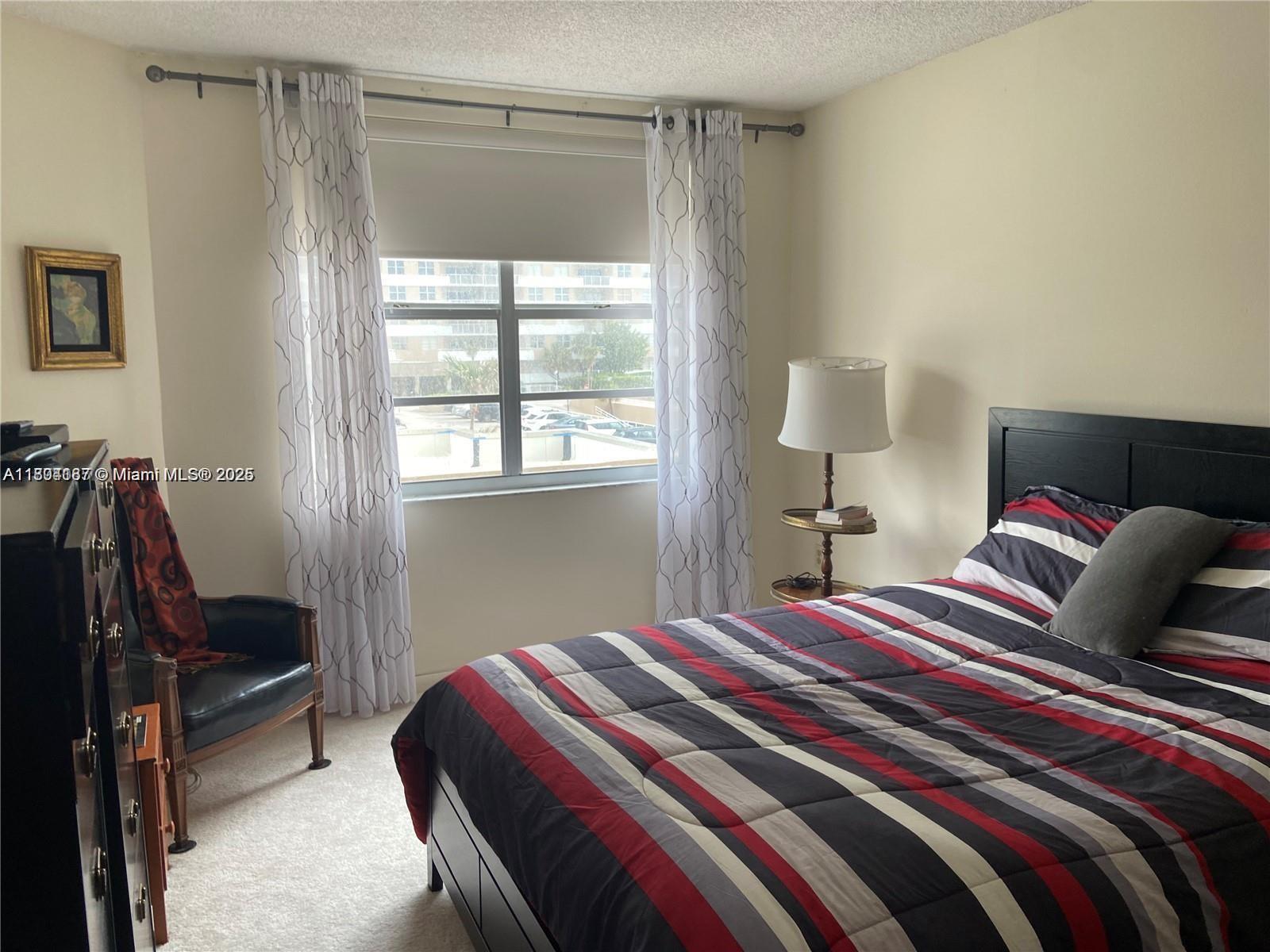A bedroom features a striped bed, a leather chair, and a window with sheer curtains — 1980 S Ocean Dr # 2B, Hallandale Beach FL 33009, HALLANDALE BEACH, FL