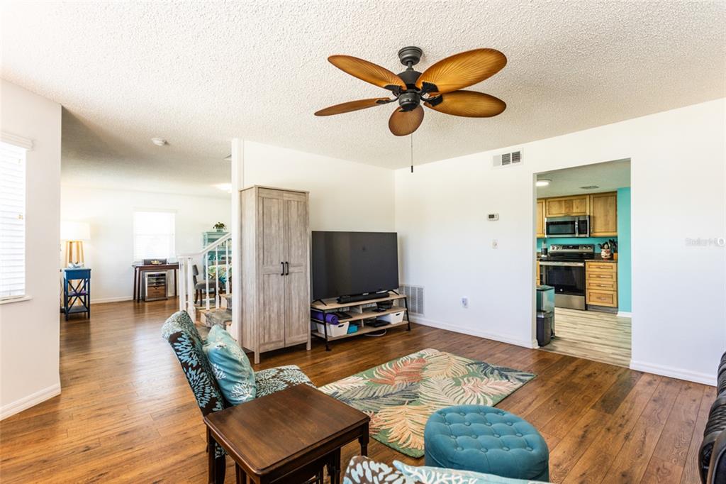 A living room with wood flooring, a ceiling fan, a television, and an adjacent kitchen — 44 FLAGLER DRIVE, PALM COAST, FL