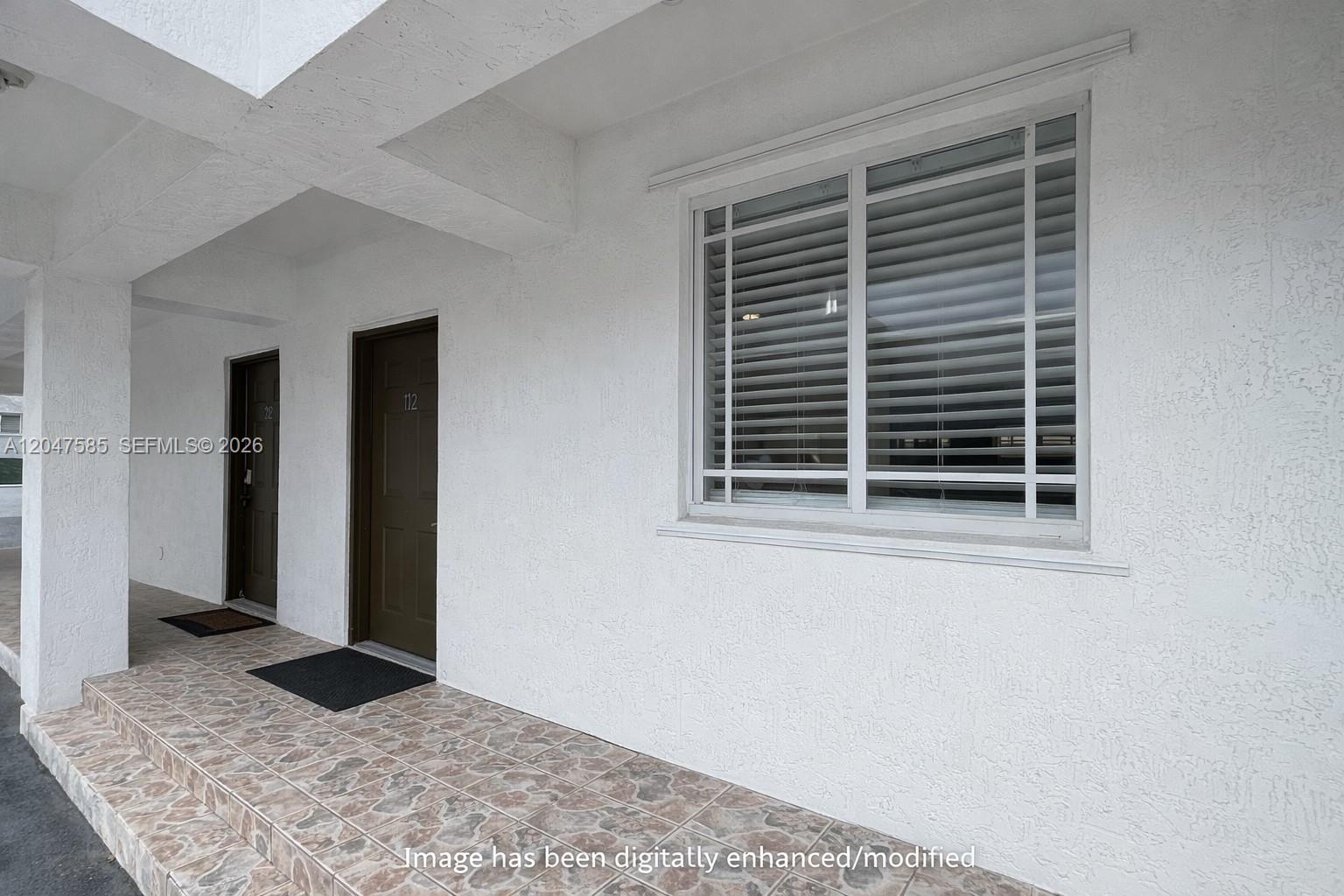 The exterior view shows a tiled walkway leading to two brown doors and a window — 318 E 6th St # 102, Hialeah FL 33010, HIALEAH, FL