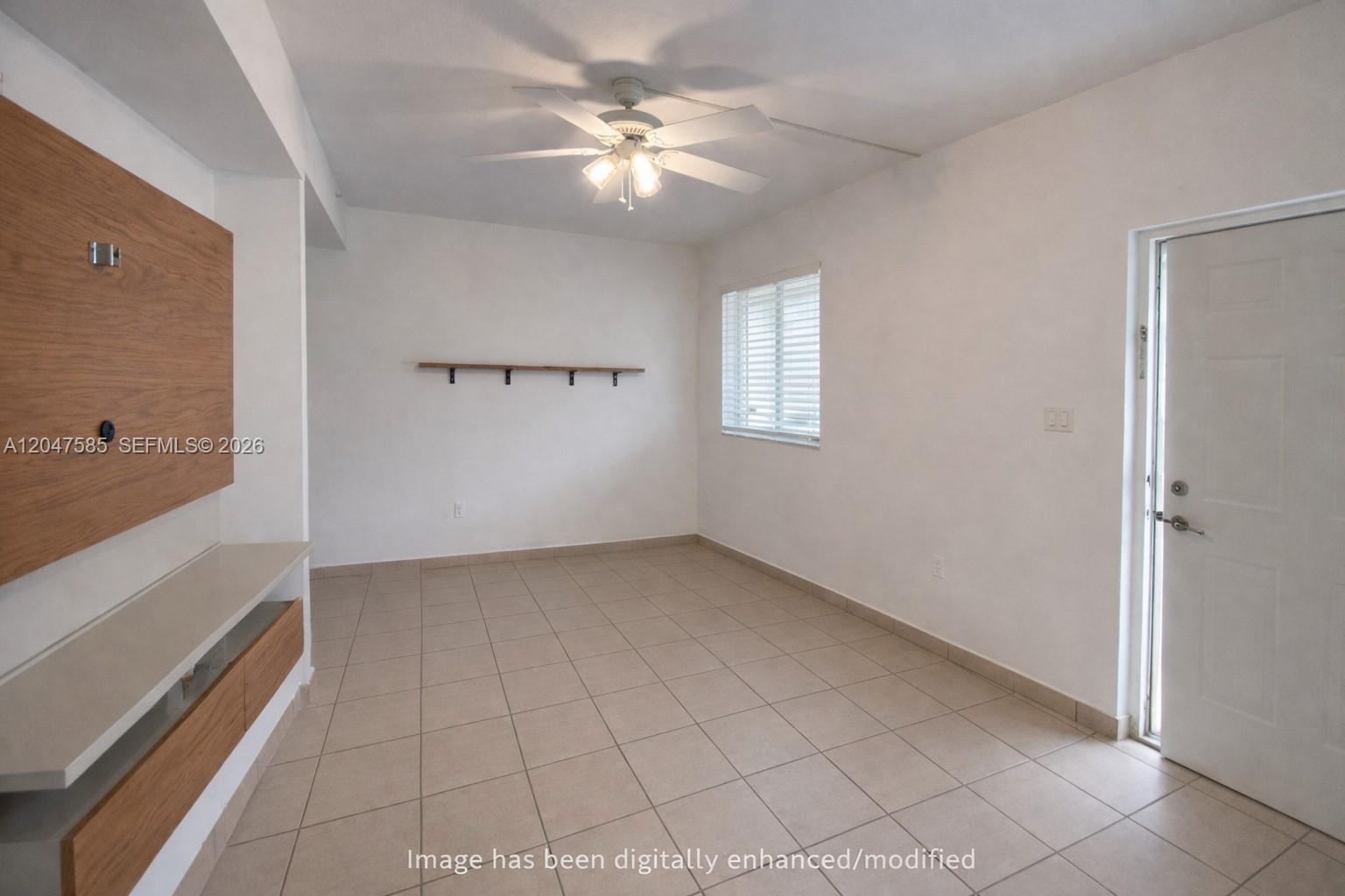 An empty room features white walls, tile flooring, a ceiling fan, and a wood-paneled wall — 318 E 6th St # 102, Hialeah FL 33010, HIALEAH, FL