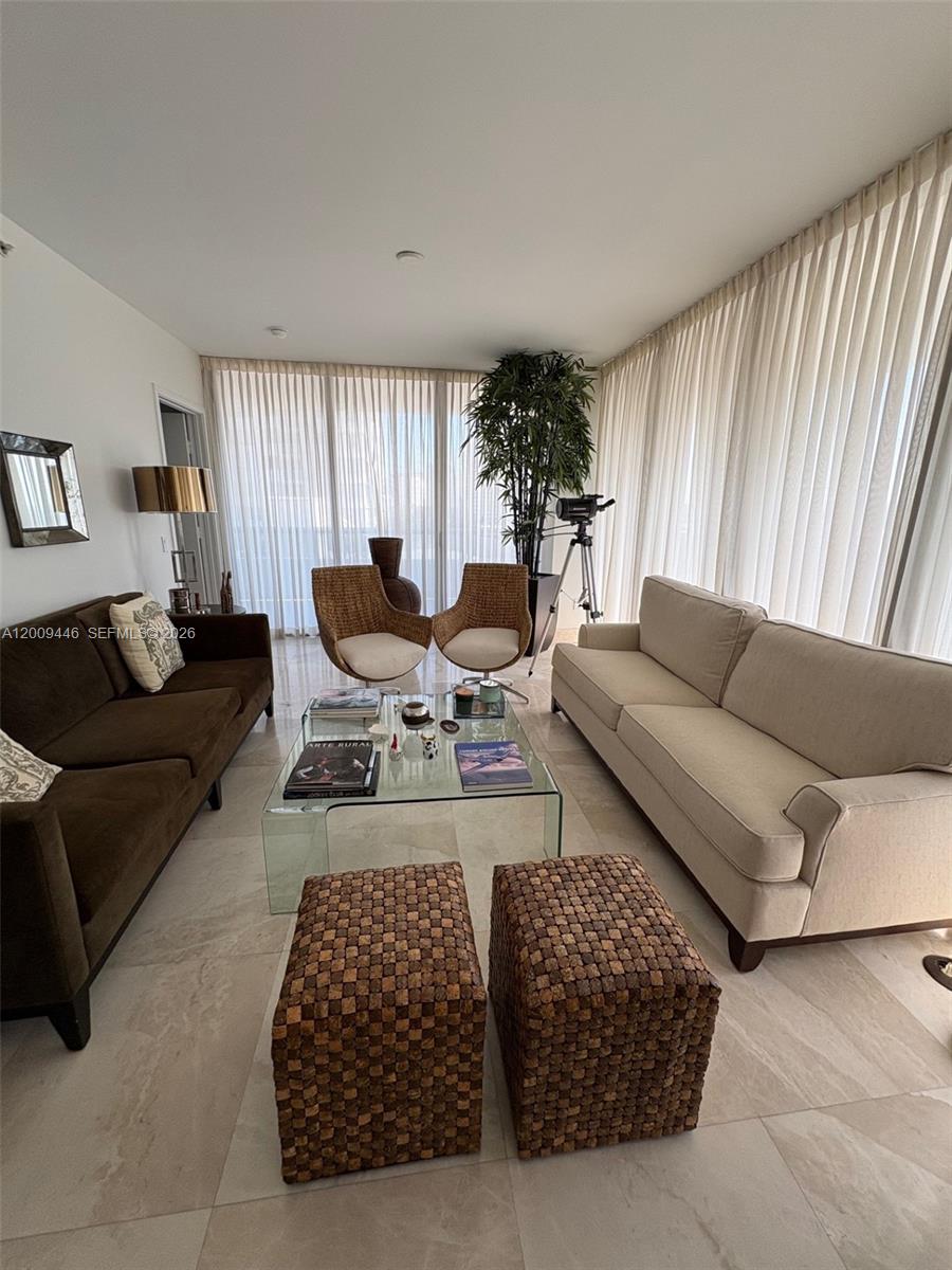 A living room features two sofas, two woven chairs, a glass coffee table, and floor-to-ceiling curtains — 5875 Collins Ave # 708, Miami Beach FL 33140, MIAMI BEACH, FL