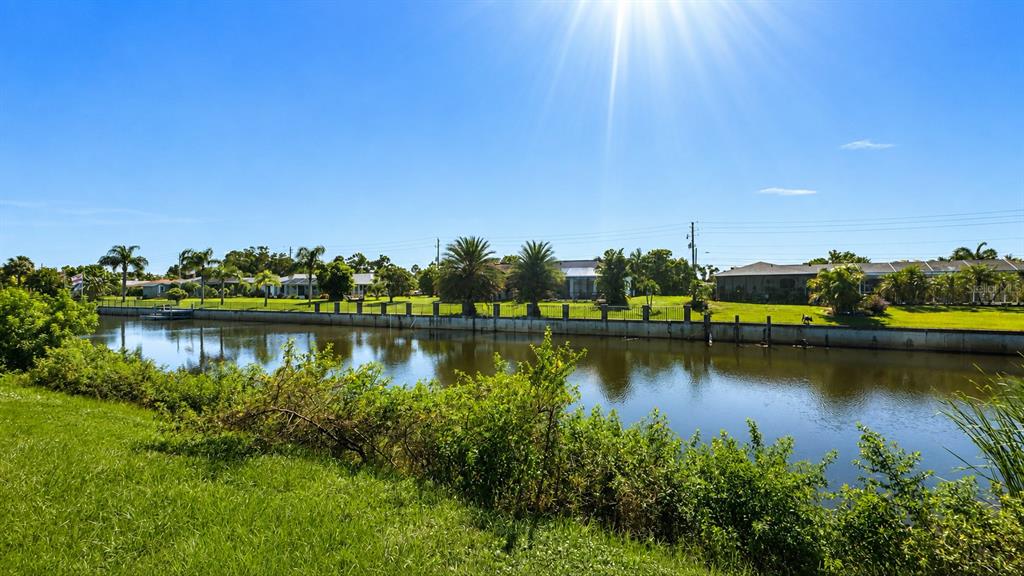 A canal separates a grassy bank from a row of houses with palm trees — 2404 ABSCOTT STREET, PORT CHARLOTTE, FL