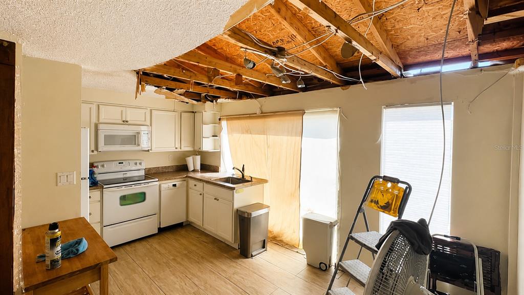 A kitchen with white cabinets and a partially demolished ceiling exposing the wooden roof structure — 2404 ABSCOTT STREET, PORT CHARLOTTE, FL