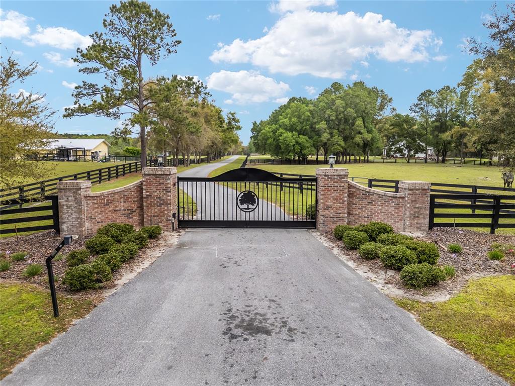 A paved driveway leads to a black metal gate flanked by brick pillars and fencing — 3595 NW 156TH DRIVE, NEWBERRY, FL