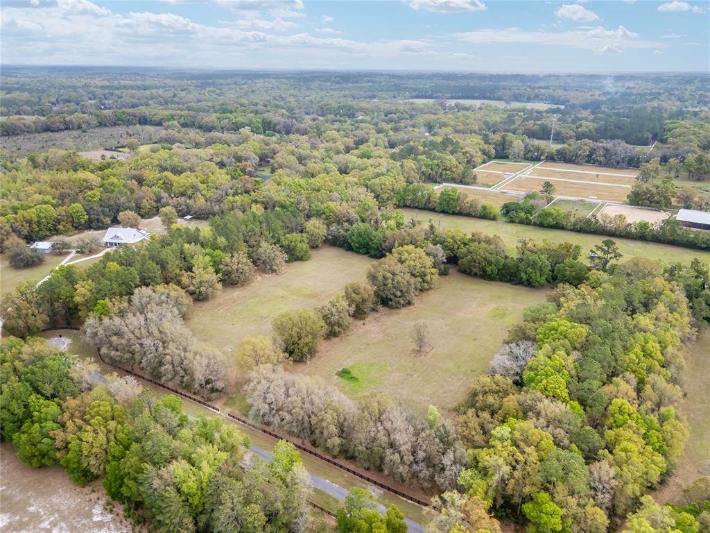 An aerial view shows a large, grassy lot surrounded by dense trees and a fence — 3595 NW 156TH DRIVE, NEWBERRY, FL