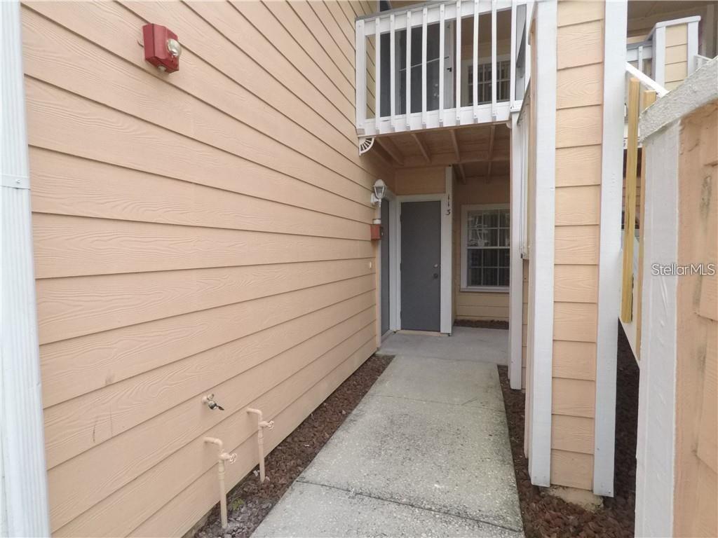 A concrete walkway leads to the entrance of a tan-sided building with a balcony above — 2010 ROYAL BAY BOULEVARD UNIT 113, KISSIMMEE, FL