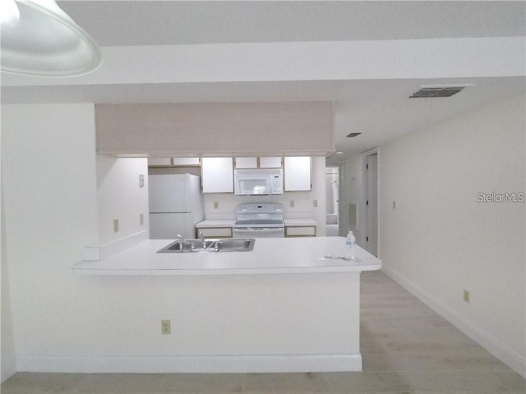 A white kitchen features a breakfast bar, white appliances, and light-colored flooring — 2010 ROYAL BAY BOULEVARD UNIT 113, KISSIMMEE, FL