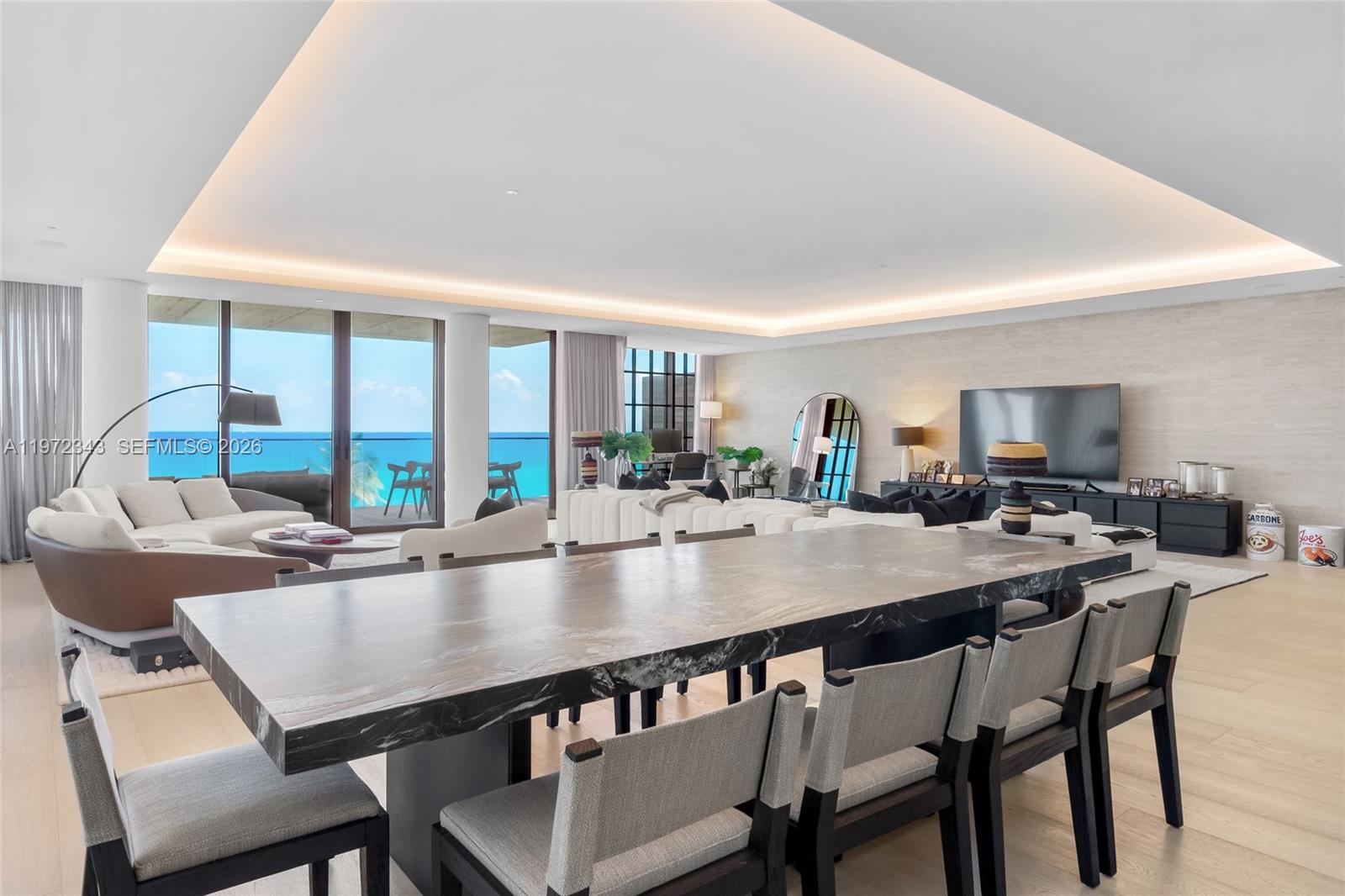 A modern dining area with a marble table overlooks a living room and ocean view — 8955 NE Collins Ave # 301, Surfside FL 33154, SURFSIDE, FL