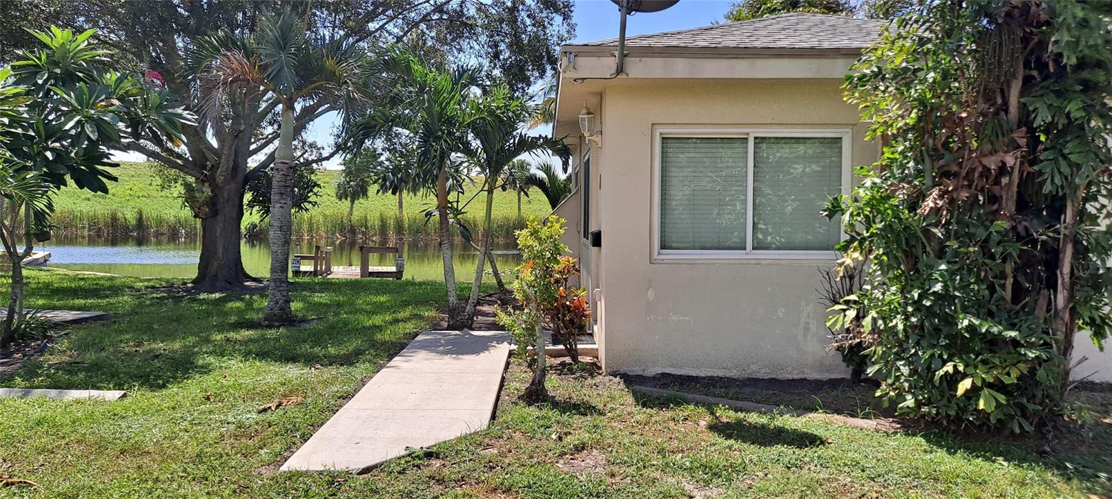 A concrete walkway leads to the side of a house near a pond and trees — 1118 Us Highway 441, Okeechobee FL 34974, OKEECHOBEE, FL