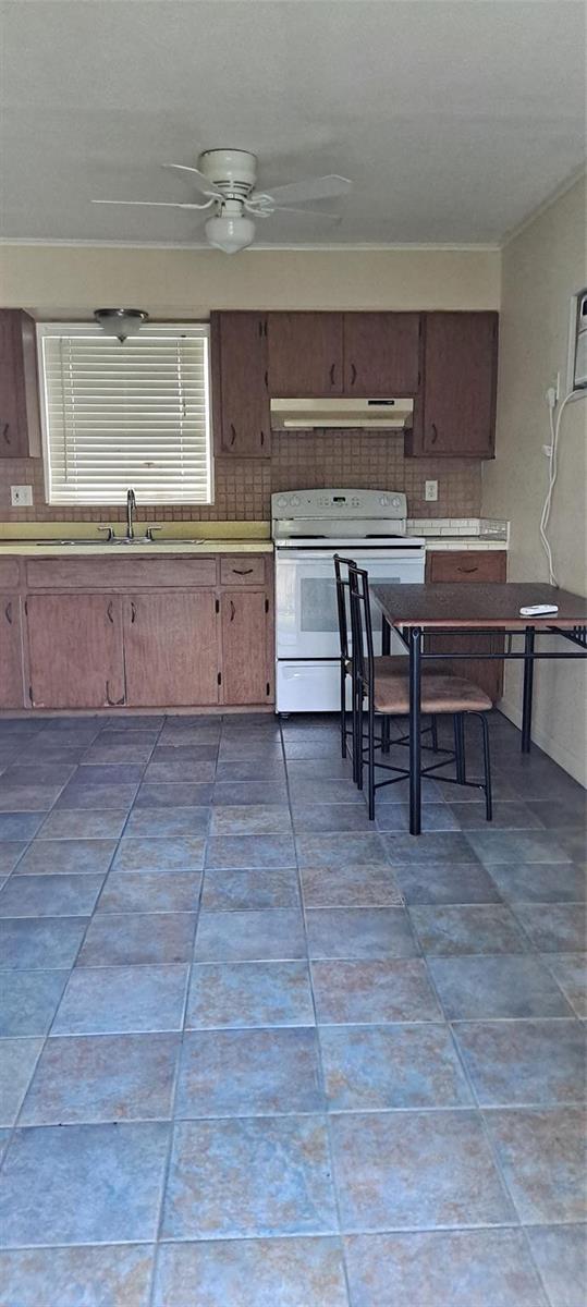 A kitchen features brown wooden cabinets, a white stove, a small dining table, and tiled flooring — 1118 Us Highway 441, Okeechobee FL 34974, OKEECHOBEE, FL