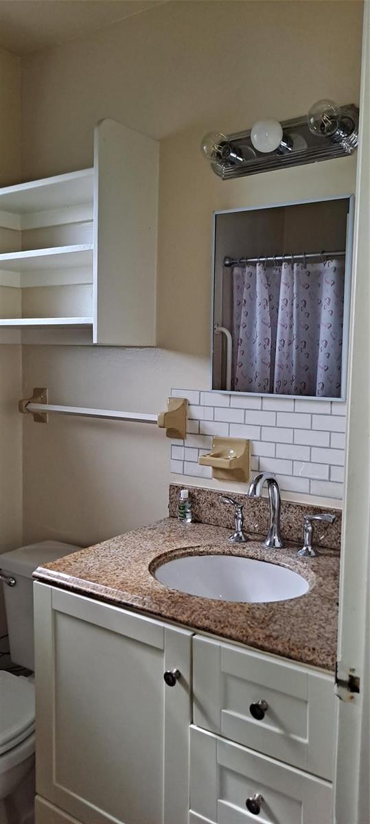 A bathroom vanity features a granite countertop, white cabinets, a subway tile backsplash, and shelving — 1118 Us Highway 441, Okeechobee FL 34974, OKEECHOBEE, FL