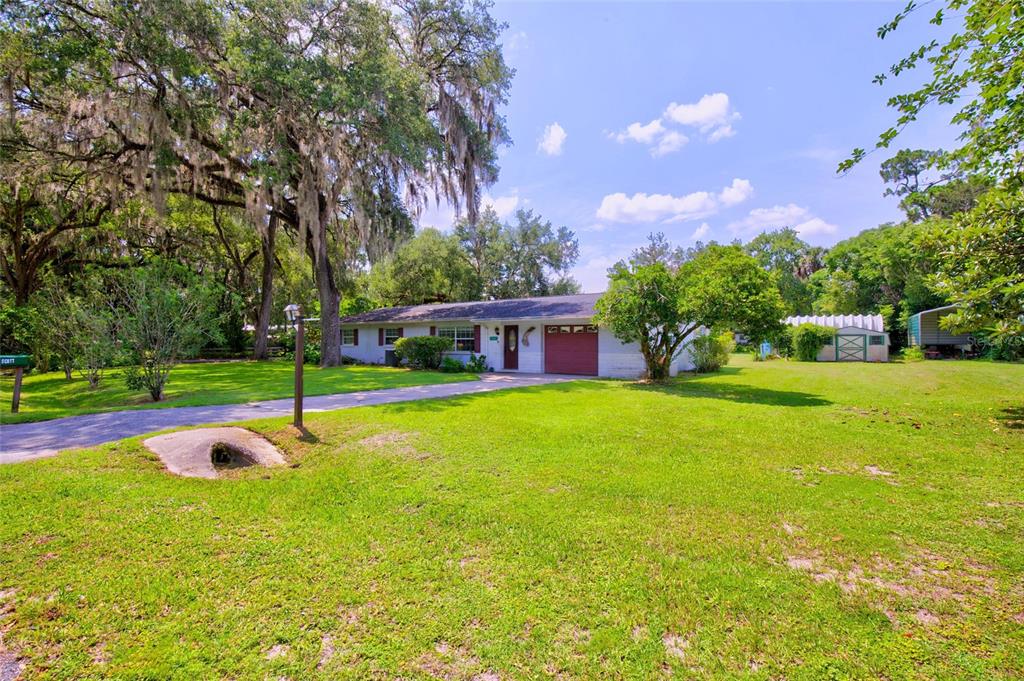 A single-story house with a red garage door sits on a large, grassy lot — 20934 THIRD AVENUE, DUNNELLON, FL