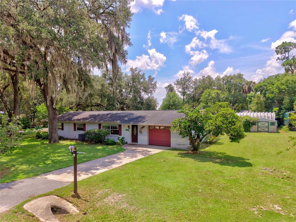 A single-story house with a red garage door and a large lawn under oak trees — 20934 THIRD AVENUE, DUNNELLON, FL