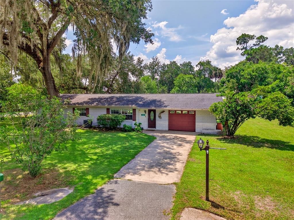A single-story house with a brick exterior, attached garage, and large trees in the yard — 20934 THIRD AVENUE, DUNNELLON, FL