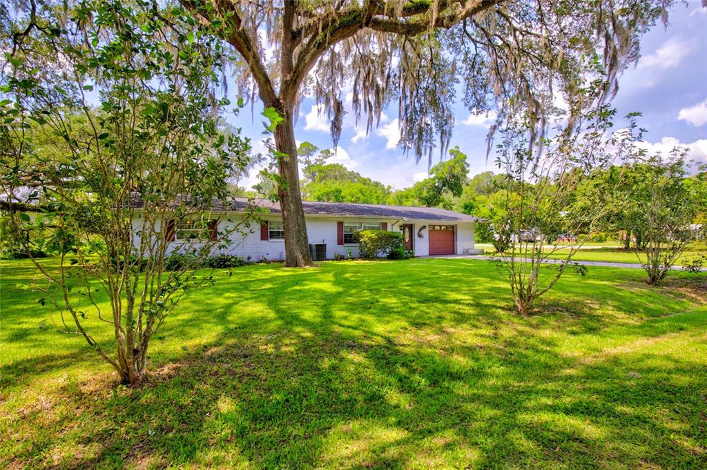 A single-story white brick house with a garage sits on a grassy lawn under trees — 20934 THIRD AVENUE, DUNNELLON, FL