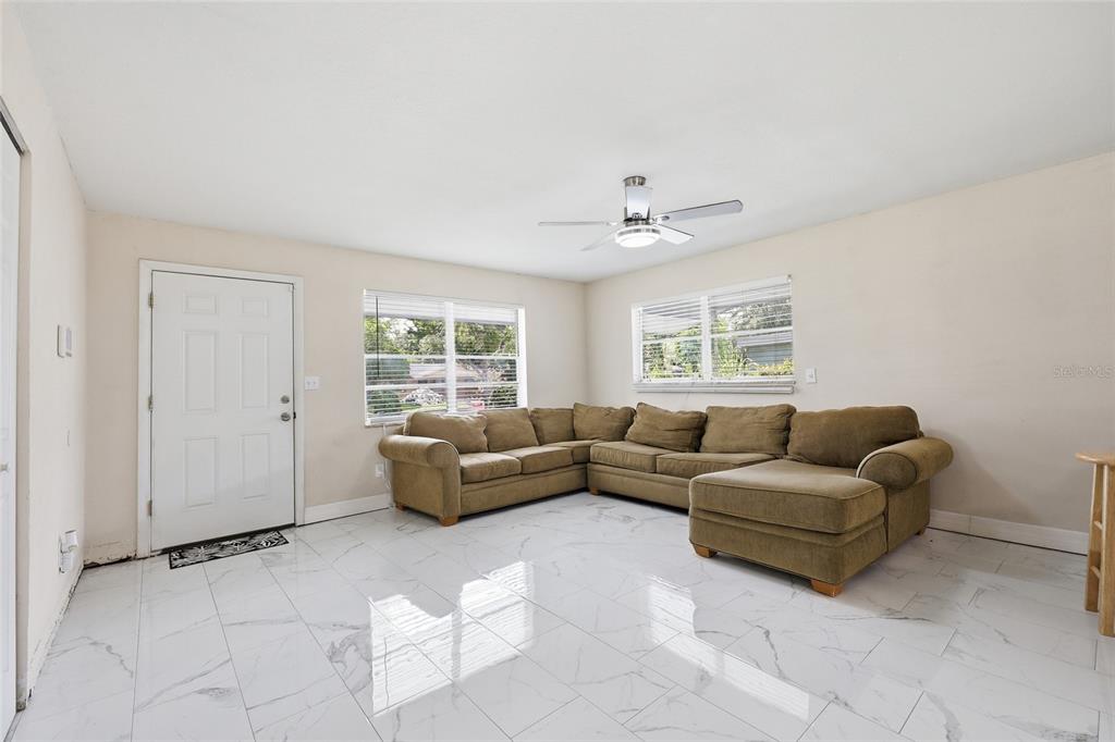 A living room features a large brown sectional sofa, white marble-look tile floors, and windows — 1651 MESSINA AVENUE, ORLANDO, FL