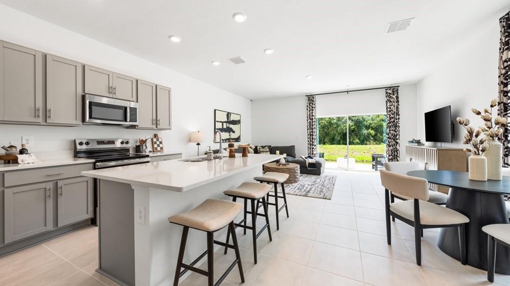 A modern open-concept kitchen and living area featuring gray cabinets, a large island, and tile — 7155 GRAND FOREST WAY, NOKOMIS, FL