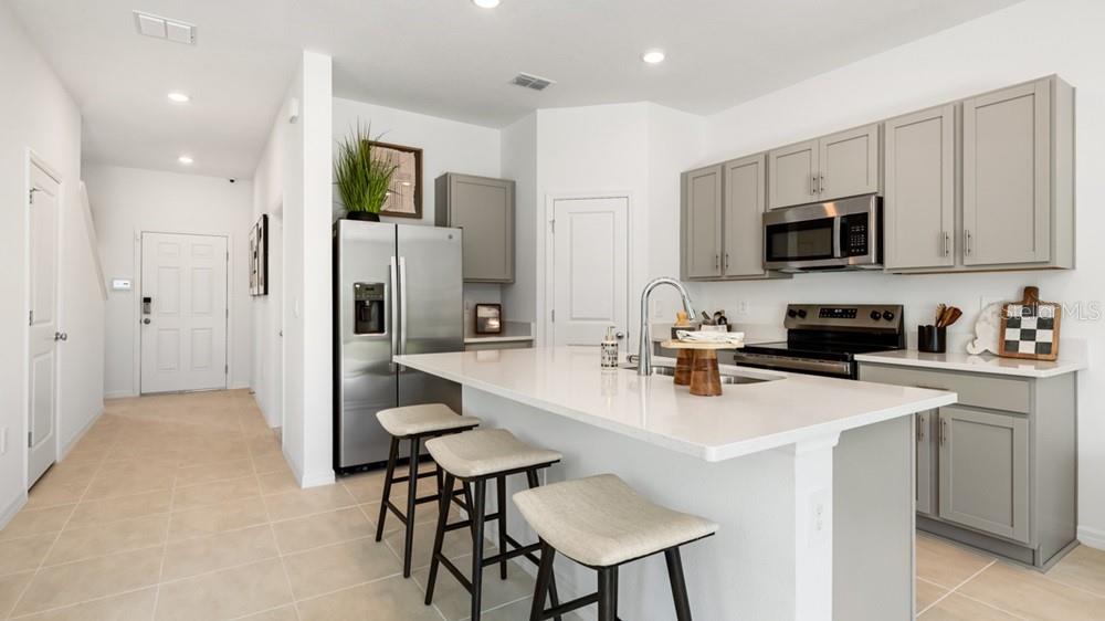 A modern kitchen features gray cabinets, stainless steel appliances, and a white quartz island — 7155 GRAND FOREST WAY, NOKOMIS, FL