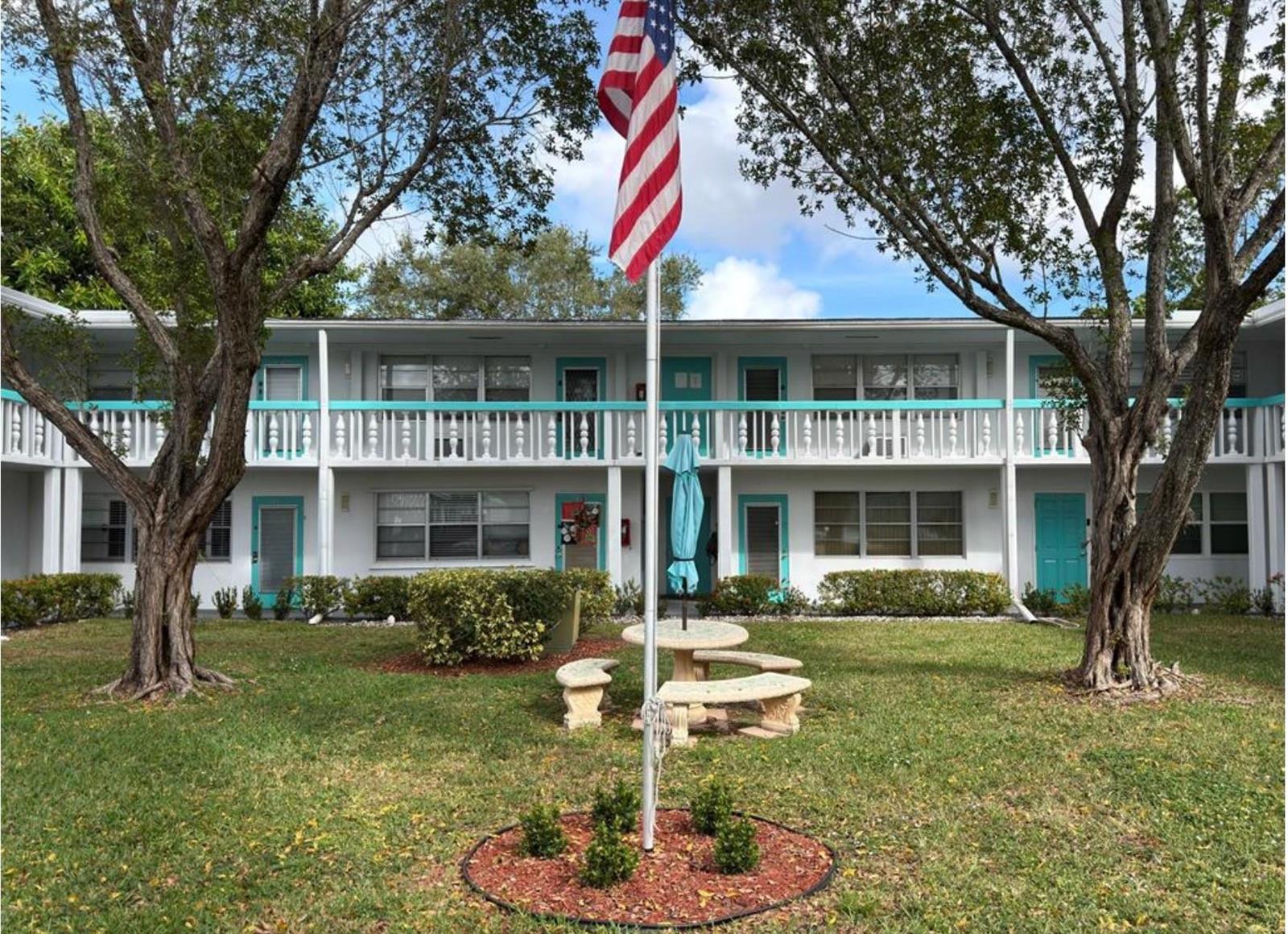 A two-story apartment building with a central courtyard, flag pole, and stone patio furniture — 295 Newport T # 295, Deerfield Beach FL 33442, DEERFIELD BEACH, FL