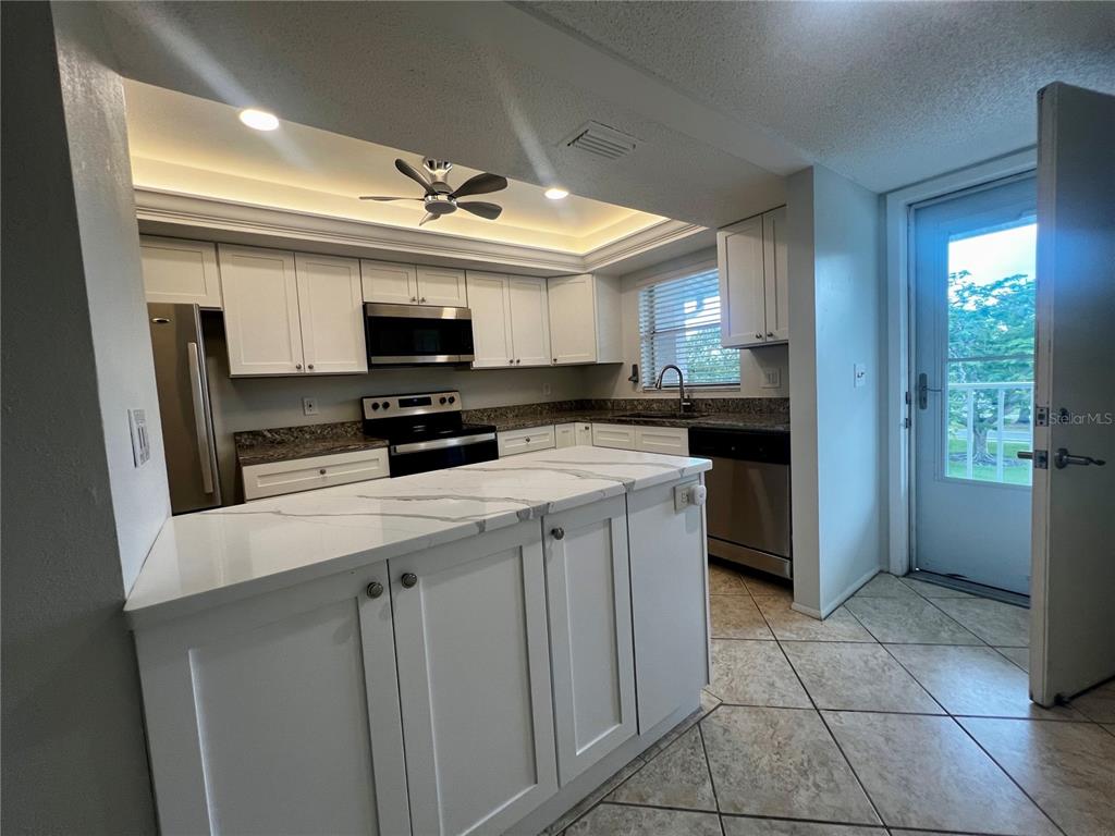 A kitchen features white cabinets, a marble-patterned island, stainless steel appliances, and tile flooring — 3981 MACEACHEN BOULEVARD UNIT 330, SARASOTA, FL