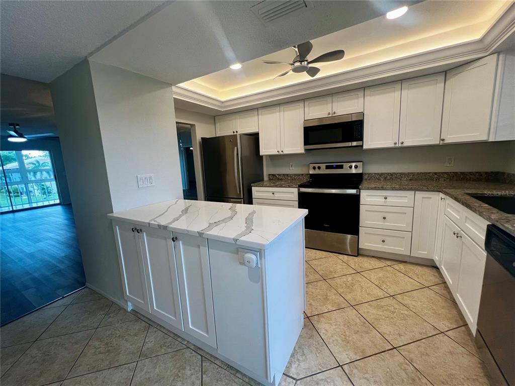 A kitchen features white cabinets, stainless steel appliances, a marble-patterned island, and tile flooring — 3981 MACEACHEN BOULEVARD UNIT 330, SARASOTA, FL