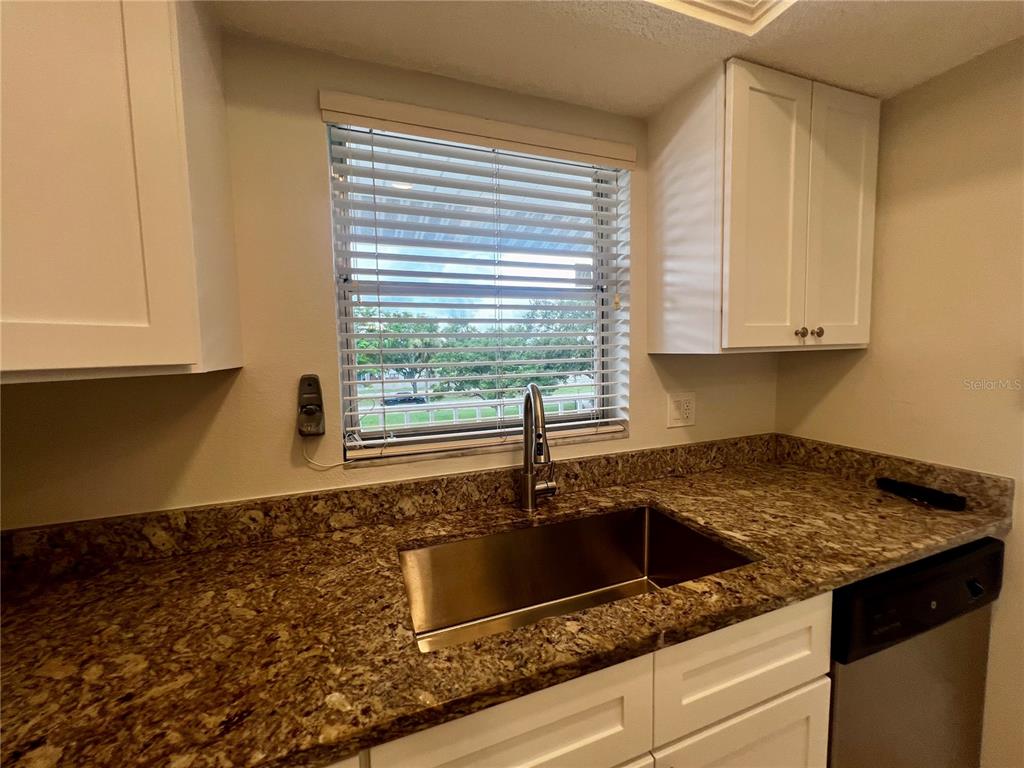 A kitchen features white cabinets, granite countertops, a stainless steel sink, and a window — 3981 MACEACHEN BOULEVARD UNIT 330, SARASOTA, FL