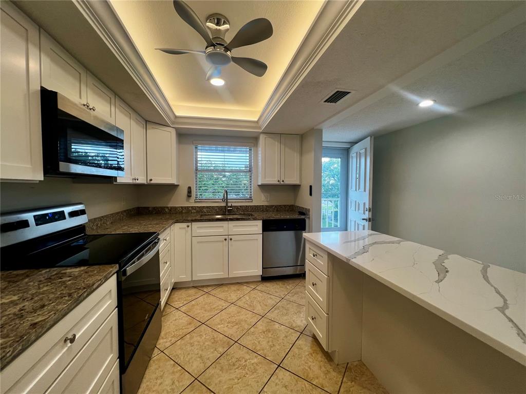 A kitchen features white cabinetry, granite countertops, a breakfast bar, and tile flooring — 3981 MACEACHEN BOULEVARD UNIT 330, SARASOTA, FL