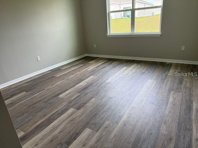 An empty room features light gray walls, white trim, and wood-look plank flooring — 3345 CURLEW AVENUE, LEESBURG, FL