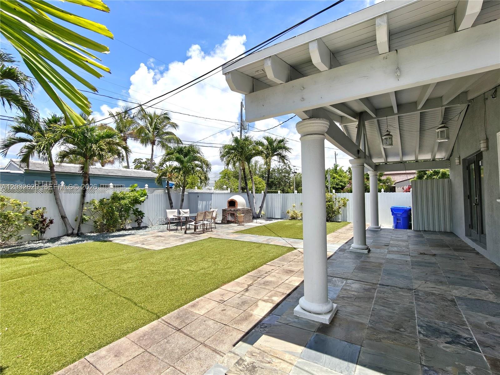 A covered patio with stone flooring overlooks a backyard featuring artificial turf and palm trees — 470 SW 25th Rd, Miami FL 33129, MIAMI, FL