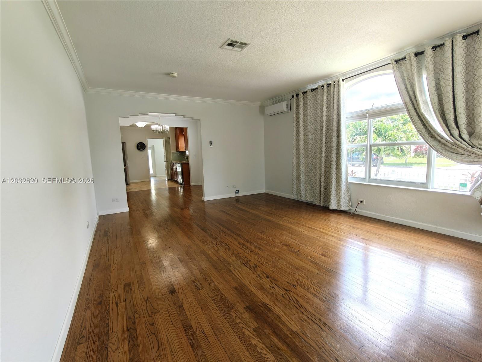 A spacious living room features hardwood floors, a large arched window, and an adjacent kitchen — 470 SW 25th Rd, Miami FL 33129, MIAMI, FL