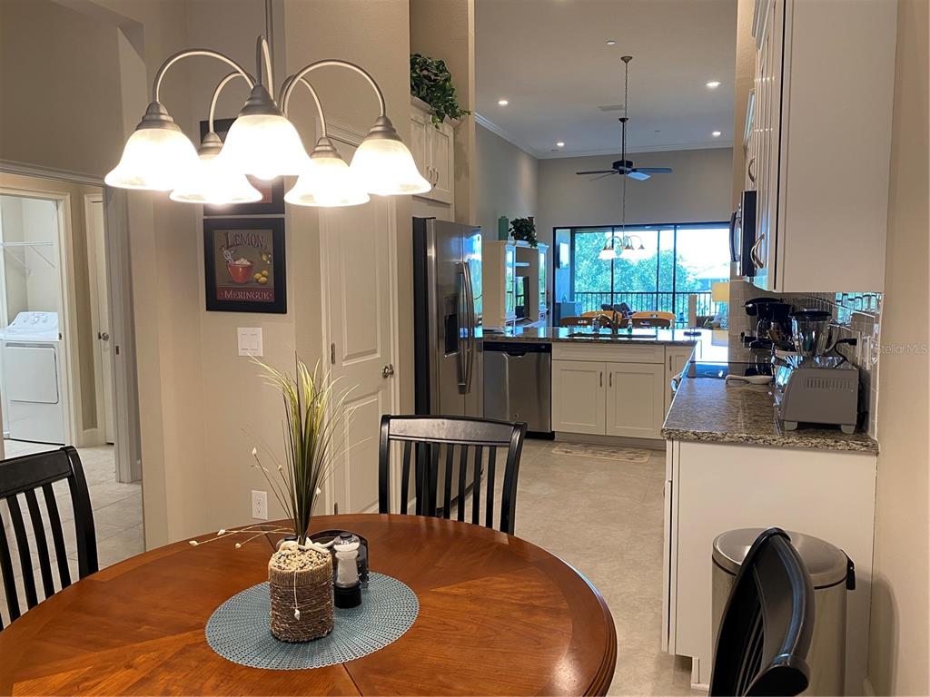 A dining area with a round wooden table overlooks a kitchen with stainless steel appliances — 13711 MESSINA LOOP UNIT 203, LAKEWOOD RANCH, FL
