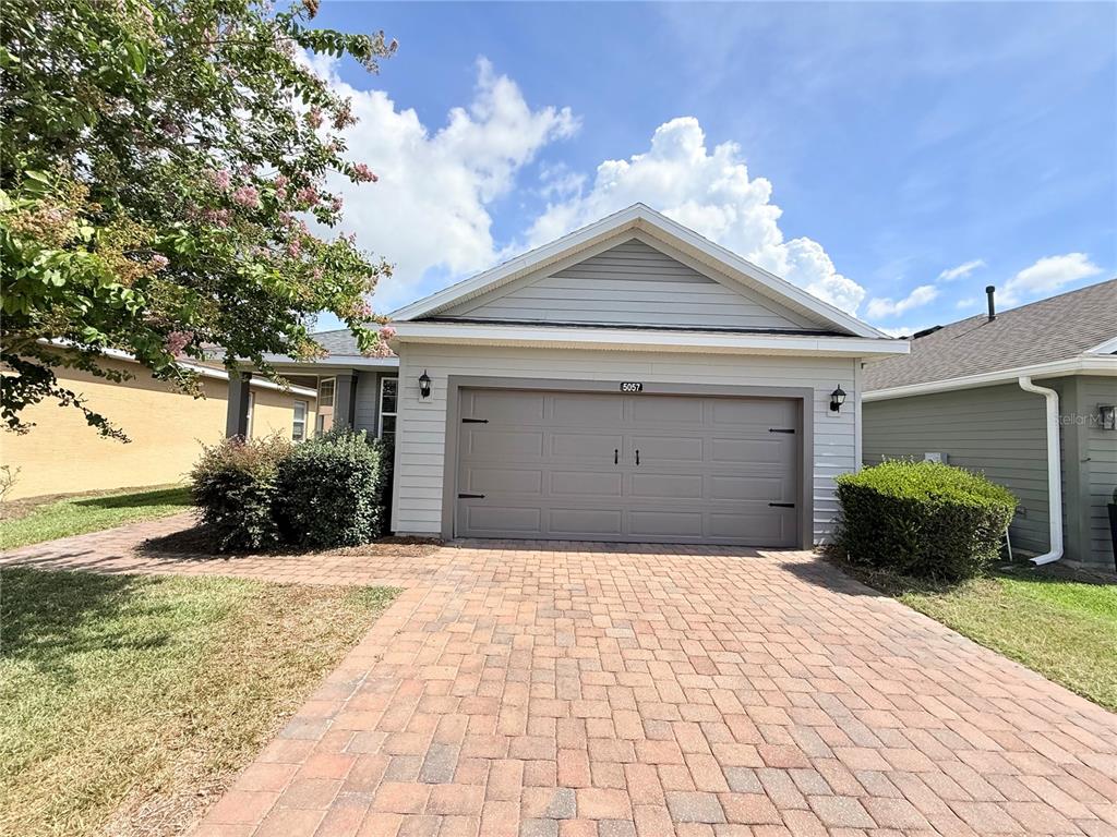 A single-story house features a gray garage door, light siding, and a brick paver driveway — 5057 NW 35TH PLACE, OCALA, FL