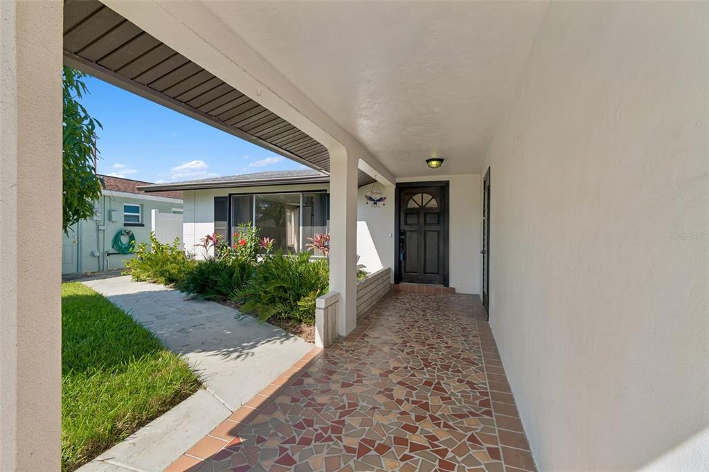 A covered entryway features a mosaic tile floor, a dark front door, and exterior landscaping — 4931 POMPANO DRIVE, NEW PORT RICHEY, FL