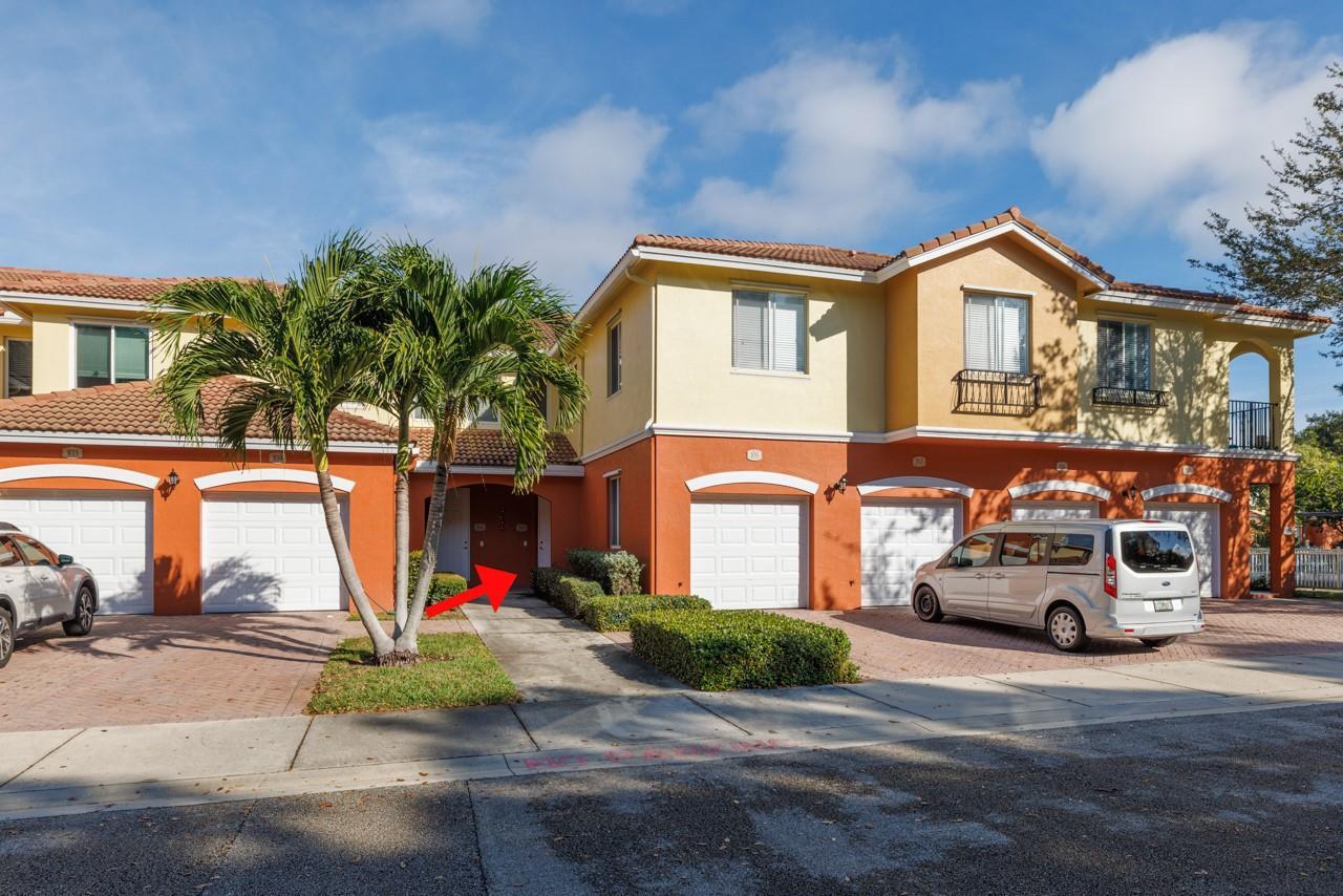 An exterior view of a two-story residential building with garages and a palm tree — 55 SE Palermo Court # 105, Stuart FL 34994, STUART, FL