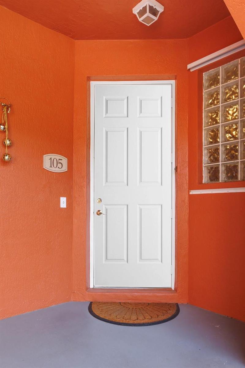 A white front door with a number 105 plaque is set in a bright orange wall — 55 SE Palermo Court # 105, Stuart FL 34994, STUART, FL