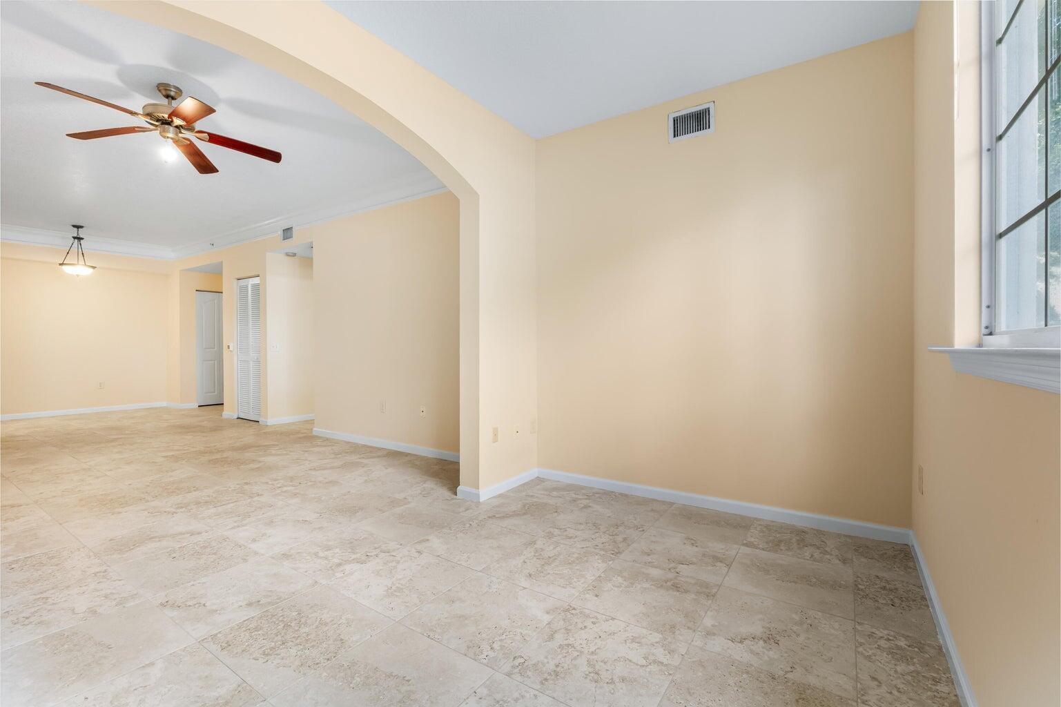 An empty room with beige walls, tile flooring, and an arched entryway to another space — 9901 Baywinds # 3105, West Palm Beach FL 33411, WEST PALM BEACH, FL