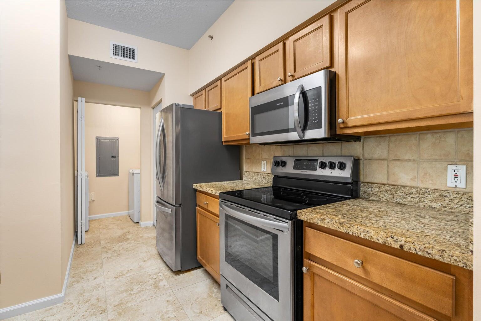 A kitchen with wood cabinets, granite countertops, stainless steel appliances, and tile flooring — 9901 Baywinds # 3105, West Palm Beach FL 33411, WEST PALM BEACH, FL